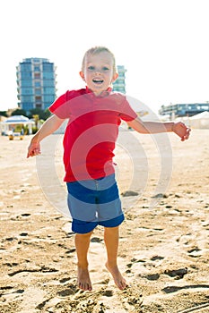 Happy beautiful smiling child jumping at the sand beach, looking at camera