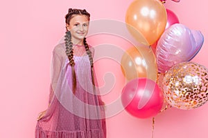 Happy and beautiful teen girl holding a bunch of colorful balloons and looking at camera with smile on pink background