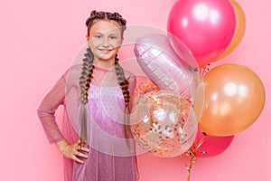 Happy and beautiful teen girl holding a bunch of colorful balloons and looking at camera with smile on pink background