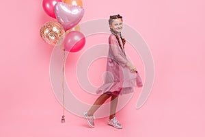 Happy and beautiful teen girl holding a bunch of colorful balloons and looking at camera with smile on pink background