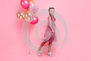 Happy and beautiful teen girl holding a bunch of colorful balloons and looking at camera with smile on pink background