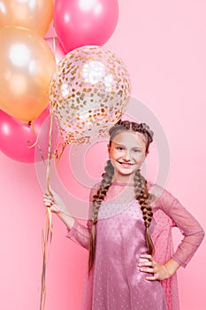 Happy and beautiful teen girl holding a bunch of colorful balloons and looking at camera with smile on pink background