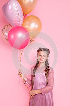 Happy and beautiful teen girl holding a bunch of colorful balloons and looking at camera with smile on pink background