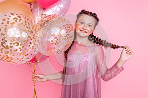 Happy and beautiful teen girl holding a bunch of colorful balloons and looking at camera with smile on pink background