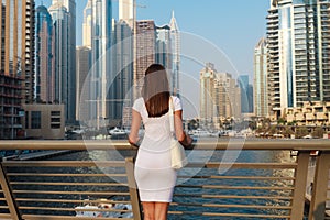 Happy beautiful unrecognizable tourist woman in fashionable summer white dress enjoying in Dubai marina in United Arab Emirates.