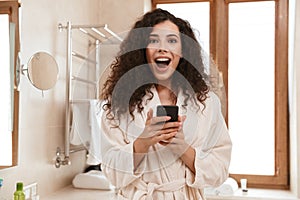 Happy beautiful woman in bathroom using mobile phone.