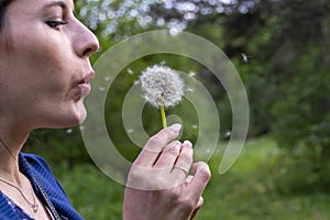 Happy beautiful woman blowing dandelion over sky background, having fun and playing outdoor, teen girl enjoying nature