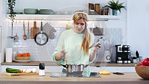 Happy beautiful woman cooking healthy food in casserole while blowing the spoon to taste the food in the kitchen at home.