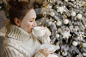 Happy beautiful woman enjoying drinking tea or coffee in living room with Christmas decor