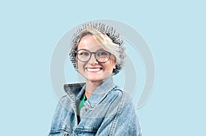 Happy beautiful woman in fashionable jeans jacket and hat on blue pastel background.