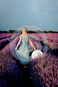 Happy and beautiful woman in a hat walking in a lavender field