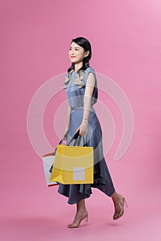 Happy beautiful woman holding many colorful shopping bags isolated on pink background