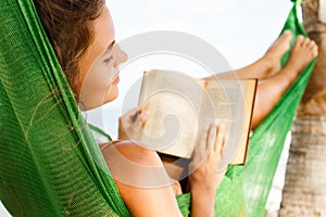 Happy and beautiful woman lying in the hammock and reading book