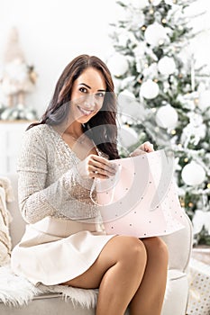 Happy beautiful woman opens light pink paper bag with X-mas gifts