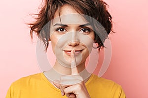 Happy beautiful woman posing  over pink wall background showing silence gesture