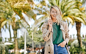 Happy beautiful woman smiling broadly, during the journey. Pretty female walking on the city street on sunny day, against palms