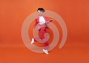 Happy beautiful woman smiling and jumping while celebrating success isolated over orange background