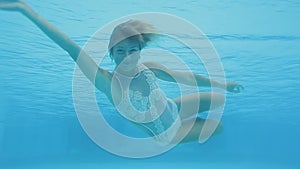 Happy beautiful woman swimming underwater in swimming pool. She smiles