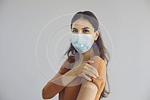 Happy beautiful woman wearing face mask shows arm after getting safe Covid 19 vaccine