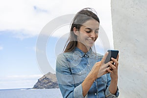 Happy beautiful woman writing or reading an email online on a smart phone on a port. Teenager playing a game in a dock on her