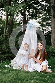 Happy beautiful woman, young mother playing with her adorable baby son, cute little boy, enjoying together a sunny warm