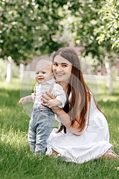 Happy beautiful woman, young mother playing with her adorable baby son, cute little boy, enjoying together a sunny warm