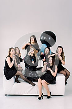 Happy beautiful women celebrating birthday or hen party, sitting on white sofa indoor and blowing soap bubbles. Birthday