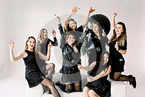 Happy beautiful women celebrating birthday or hen party, sitting on white sofa indoor and blowing soap bubbles. Birthday