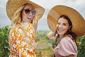 happy beautiful women in elegant dresses and wide brimmed straw hats are smiling and looking at the camera photo