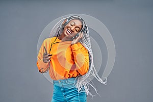 Happy beautiful young african american woman with mobile phone listening to music and dancing over grey background