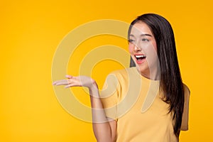 Happy beautiful young asian woman with yellow background holding copy space imaginary on beauty palm for insert advertisement,