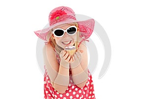 Happy, beautiful young blonde girl in big pink floppy hat and white framed sunglasses excitedly holding up a cup cake. Isolated on