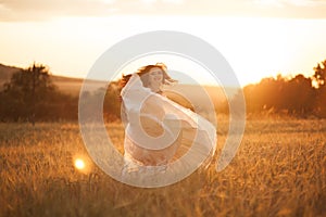 Happy beautiful young bride outside on a summer meadow at the sunset