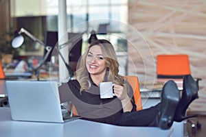 Happy beautiful young business woman sitting and talking on cell phone in office