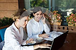 Happy beautiful young businesswomen working on laptop and drinking coffee