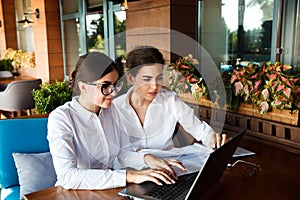 Happy beautiful young businesswomen working on laptop in street cafe outdoor