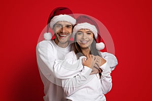 Happy Beautiful Young Couple In Santa Hats Embracing And Smiling At Camera