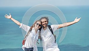 Happy beautiful young couple of travelers man and woman on top of a mountain with ocean view. Romantic travels, honeymoon