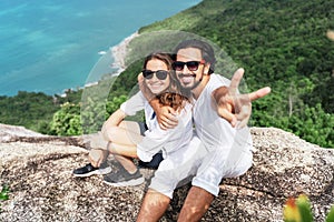 Happy beautiful young couple of travelers man and woman on top of a mountain with ocean view. Romantic travels, honeymoon