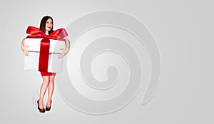 Happy Beautiful Young Girl in Red Dress Keeps in Hands Big White Gift Box with Red Ribbon on Light Background. Christmas Holiday C