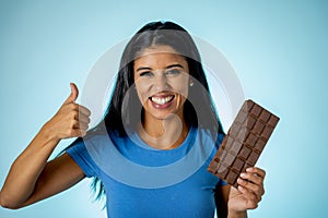 Happy beautiful young latin woman holding a big bar of chocolate with crazy excited face expression in sugar addiction and