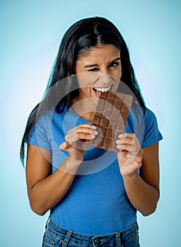 Happy beautiful young latin woman holding a big bar of chocolate with crazy excited face expression in sugar addiction and