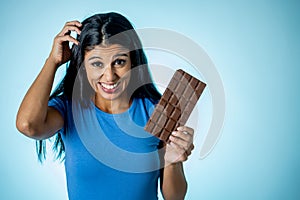 Happy beautiful young latin woman holding a big bar of chocolate with crazy excited face expression in sugar addiction and