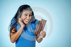 Happy beautiful young latin woman holding a big bar of chocolate with crazy excited face expression in sugar addiction and