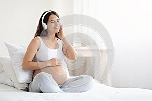Happy beautiful young pregnant woman listening to music in headphones