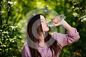 Happy beautiful young thirsty woman drinking water from transpar