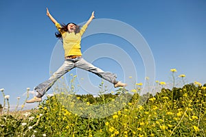 Happy and beautiful young woman in a bright yellow sweater and blue jeans jumping high in a sunny summer field