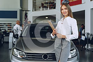 Happy beautiful young woman car dealer in showroom