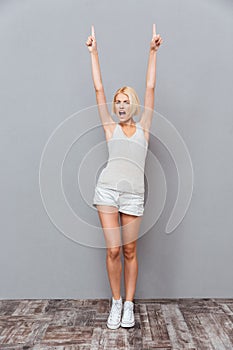 Happy beautiful young woman celebrating success and pointing up