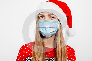 Beautiful young woman in Santa Claus hat and in a medical protective mask on her face, on a white background, Celebrating New Year